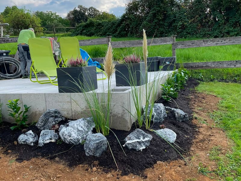 Neu angelegtes Gartenbeet mit Ziergräsern und Natursteinen neben einer Terrasse