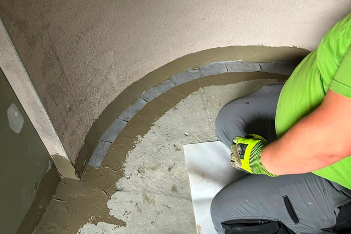 Mitarbeiter zieht eine Hohlkehle mit Dichtband und Dichtschlämme in einer gerundeten Duschnische